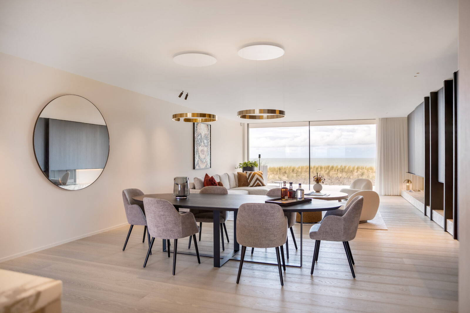 Eetkamer met ronde spiegel aan de muur, een zwarte eettafel met stoelen en gouden hanglampen boven de tafel.