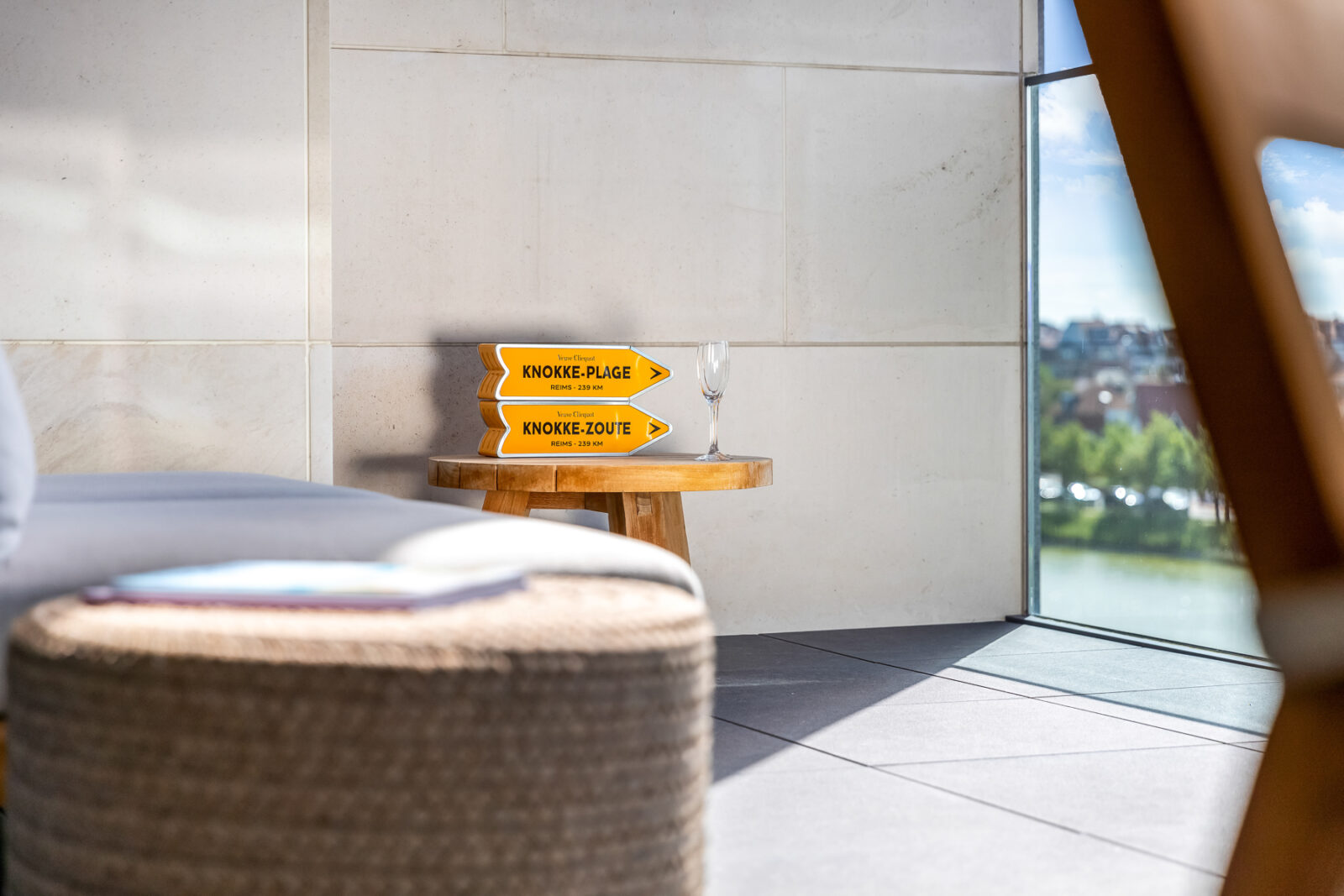 Detailopname van een houten bijzettafel met boeken en een glas, verlicht door zachte zonnestralen op een stijlvol balkon in Knokke.