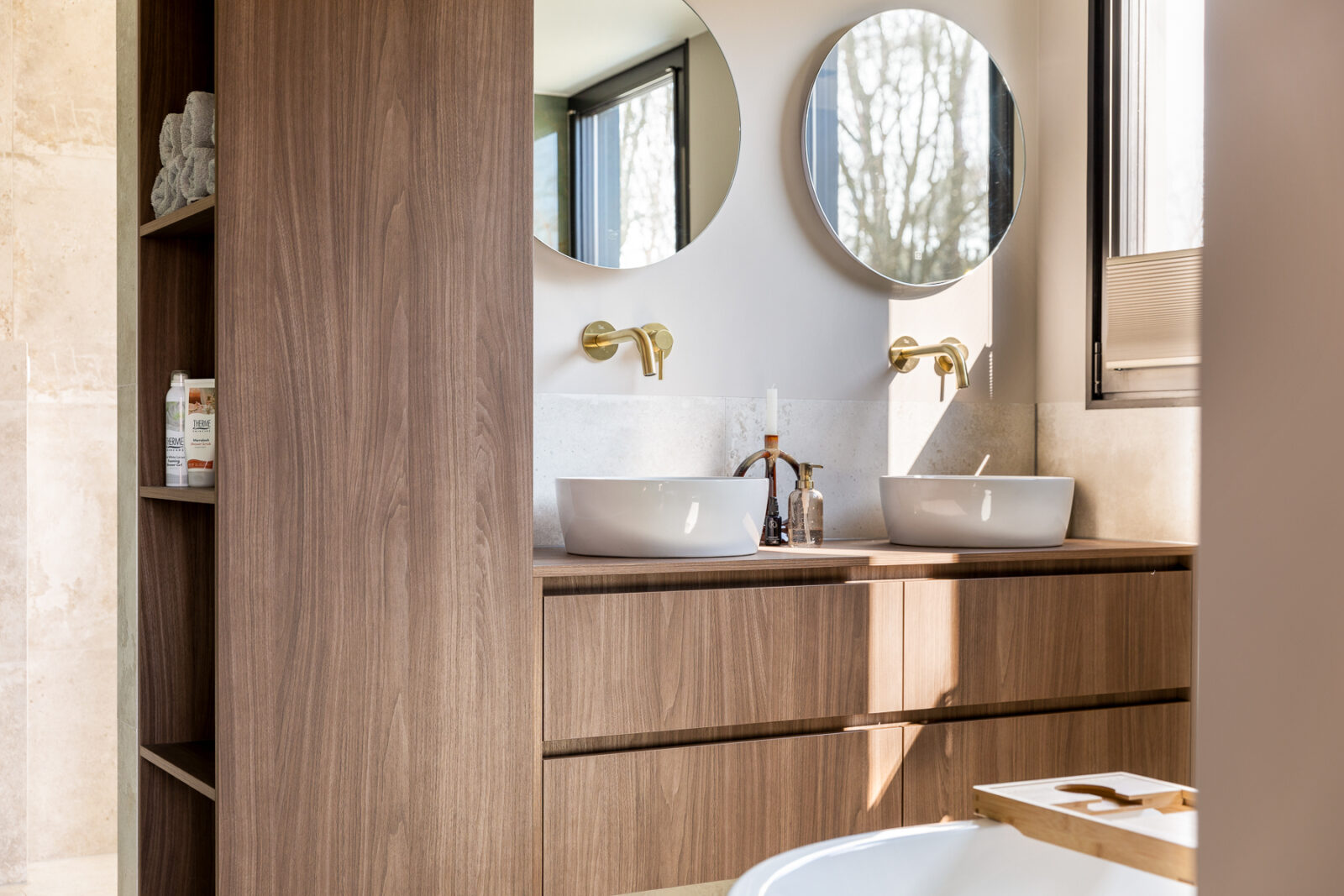 Gestylde moderne badkamer met maatwerk wastafelmeubel in walnoot, keramieken waskommen en messing kranen.