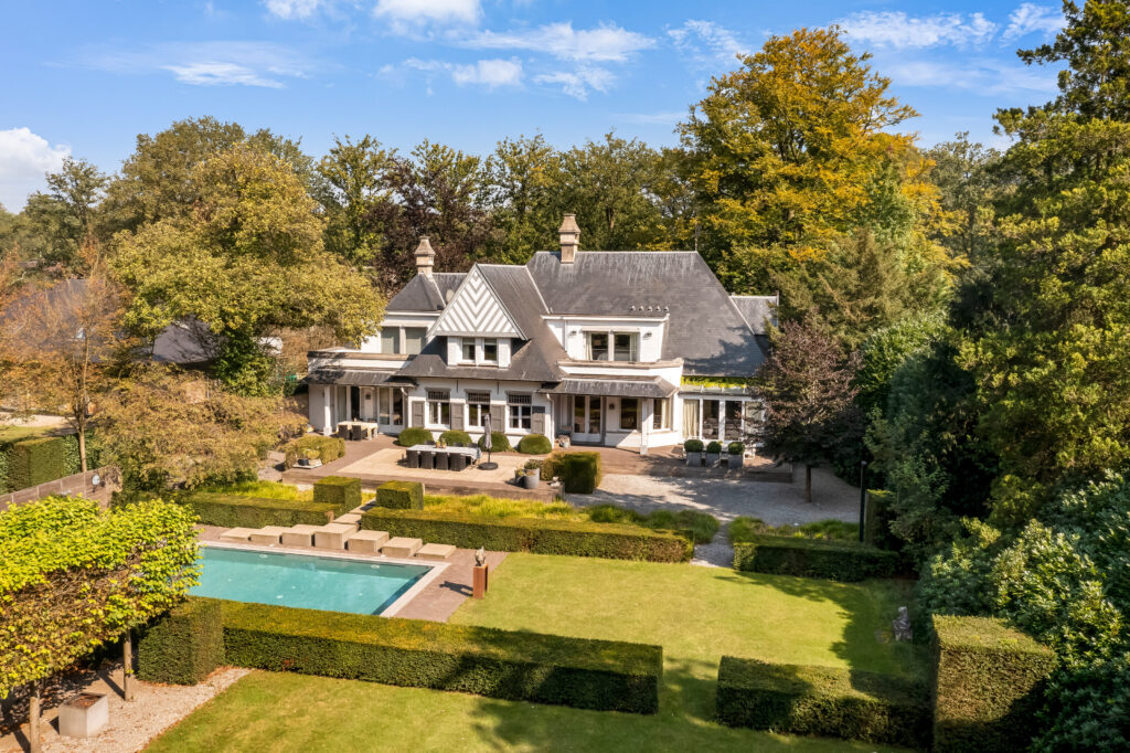 dronefotografie van een grote, luxe villa met tuin onder architectuur, een zwembad volledig omringd door bomen met daardoor veel privacy.